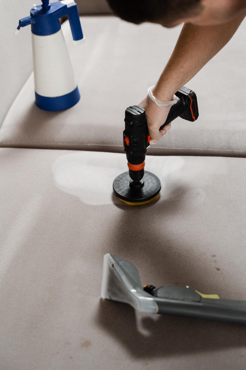 Une personne en gants effectue un nettoyage professionnel d'un canapé en tissu beige à l'aide d'un équipement spécialisé.