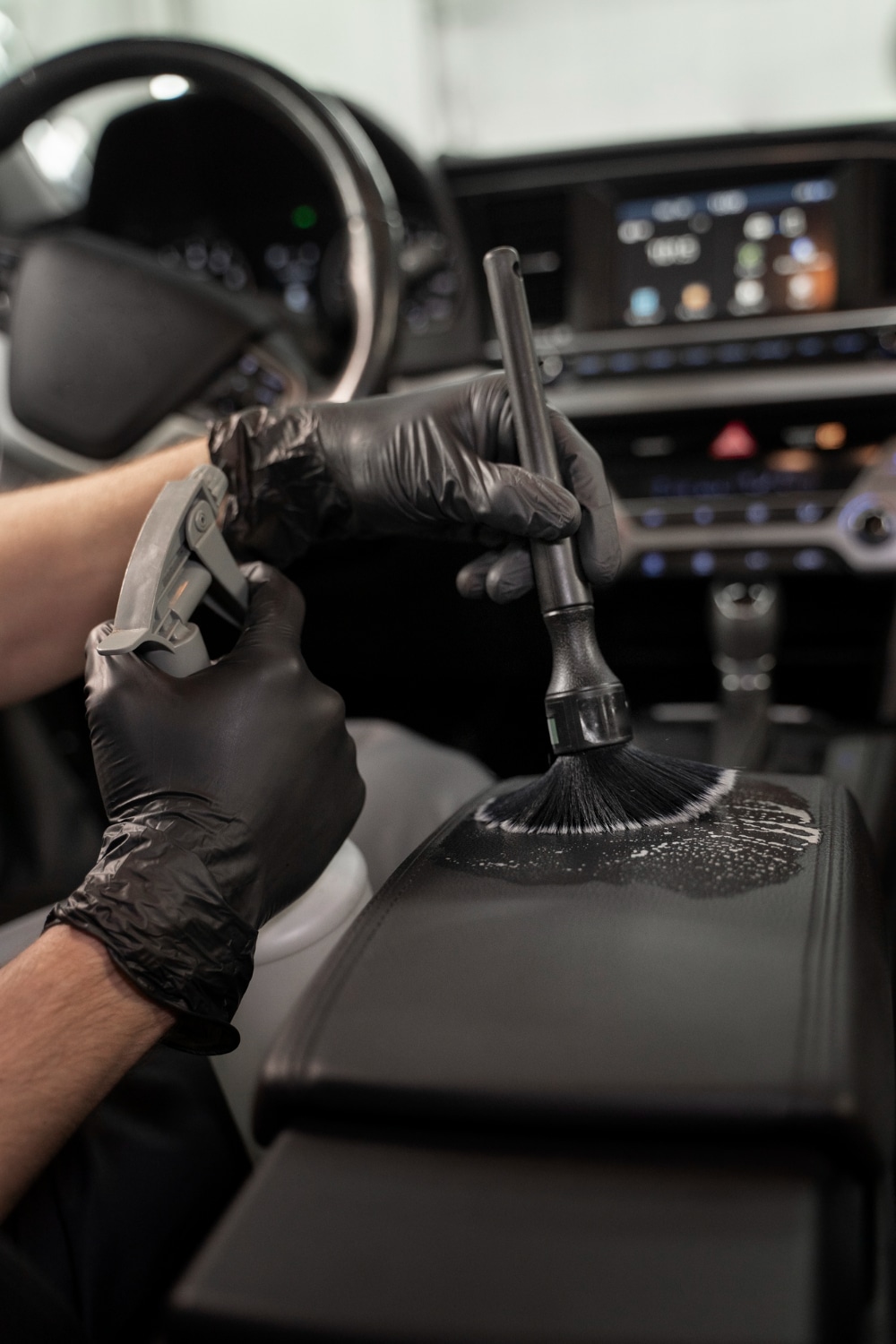 Nettoyage précis d'un tableau de bord de voiture avec une brosse à poils noirs par une main en gant noir.