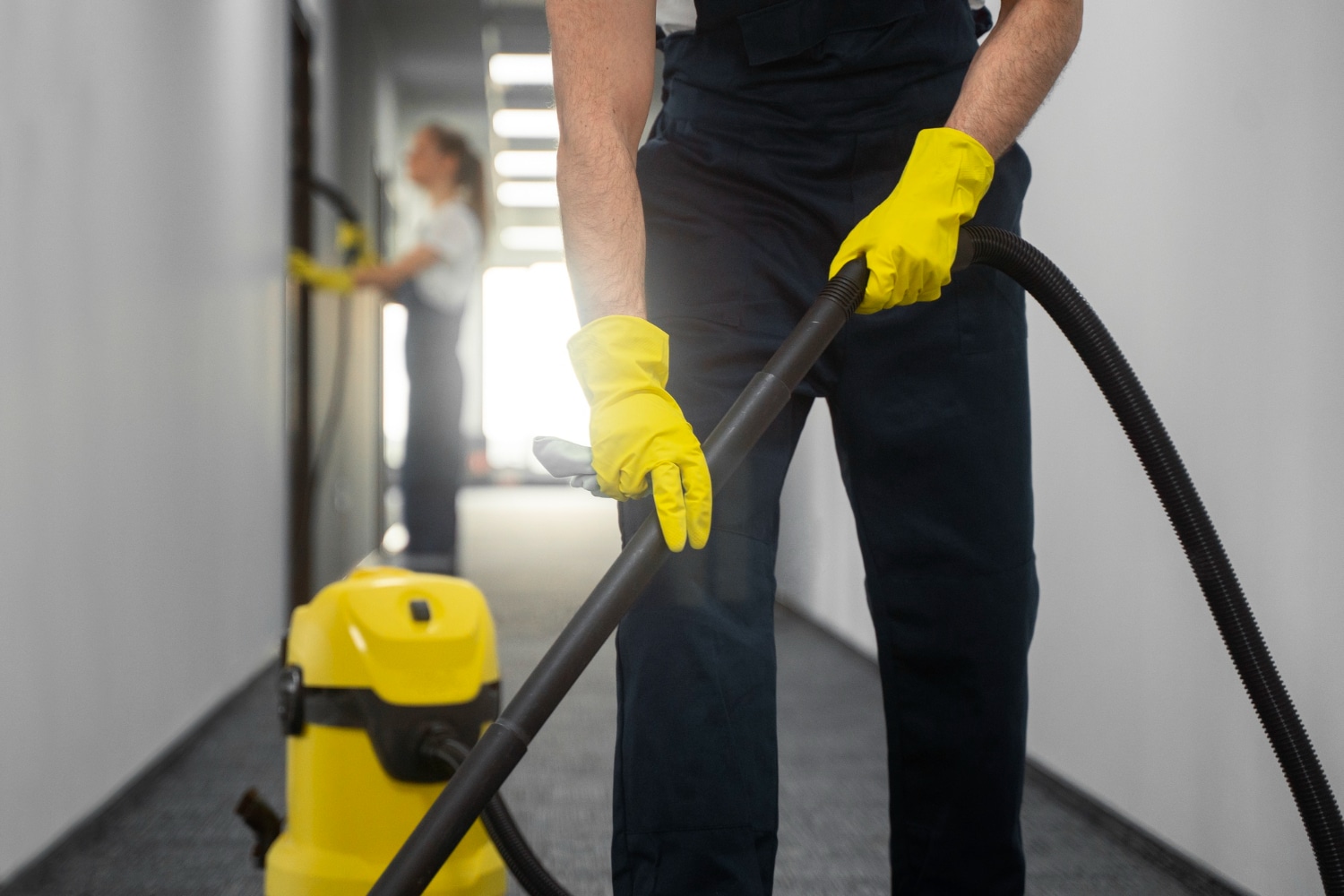 Personne en tenue de travail utilisant un aspirateur professionnel dans un couloir d'immeuble.